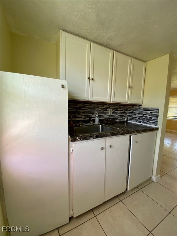 Kitchen featuring freestanding refrigerator, white cabinetry, light tile patterned floors, decorative backsplash, and dark stone countertops