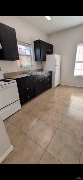 Kitchen featuring dark cabinetry, white appliances, light tile patterned floors, and plenty of natural light