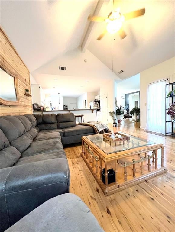 Living area featuring wood walls, beam ceiling, light wood finished floors, a ceiling fan, and high vaulted ceiling