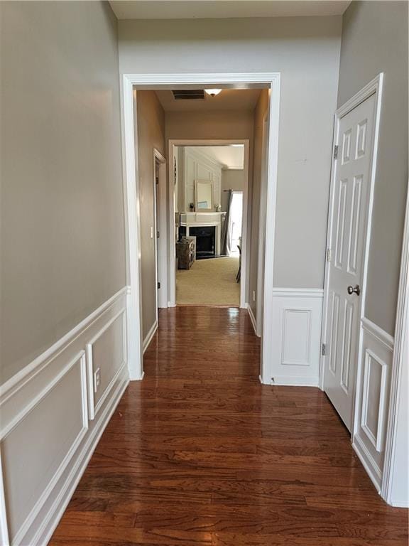 Corridor with a decorative wall, wainscoting, and dark wood finished floors
