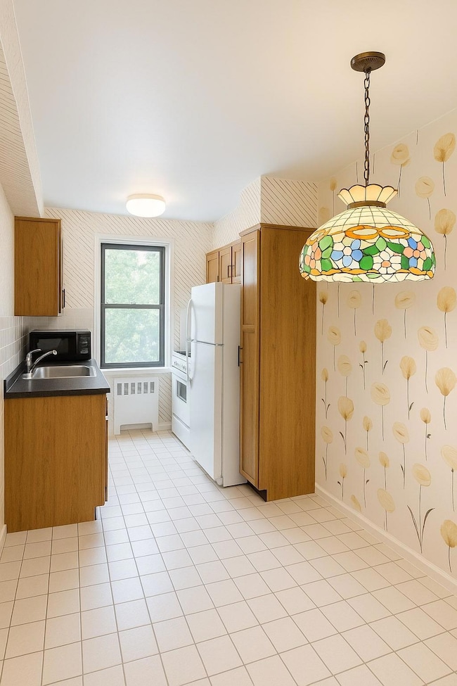 Kitchen featuring freestanding refrigerator, radiator heating unit, brown cabinets, dark countertops, and hanging light fixtures