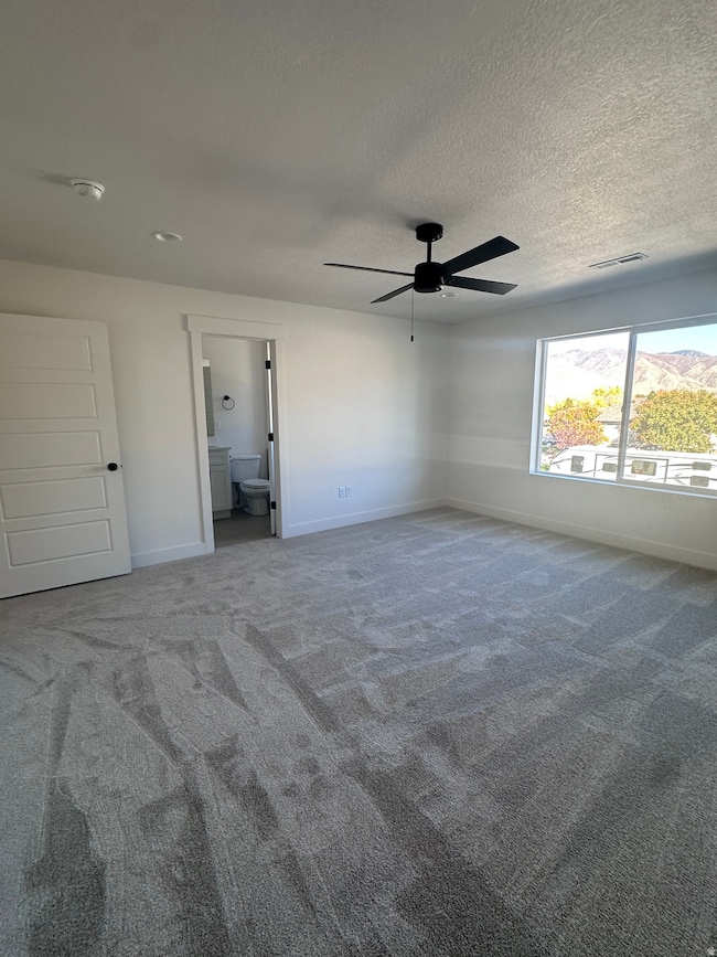 Unfurnished bedroom featuring carpet floors, a ceiling fan, connected bathroom, and a textured ceiling