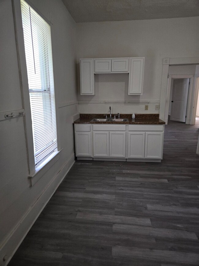 Kitchen featuring a sink, white cabinetry, dark countertops, baseboards, and dark wood-style flooring