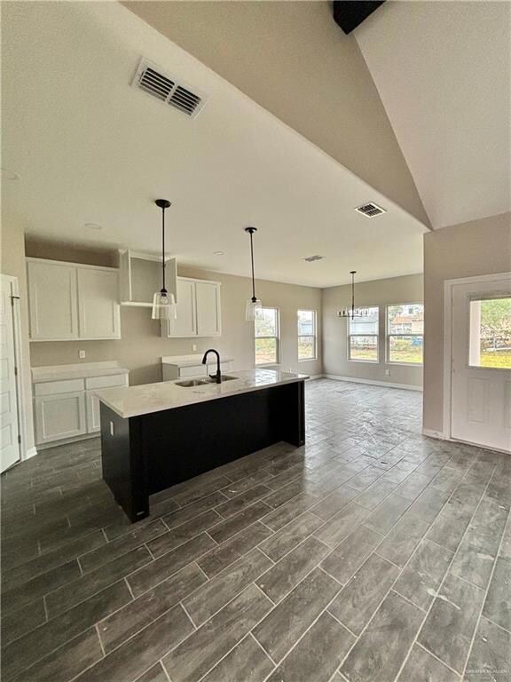 Kitchen with a wealth of natural light, an island with sink, white cabinets, and sink