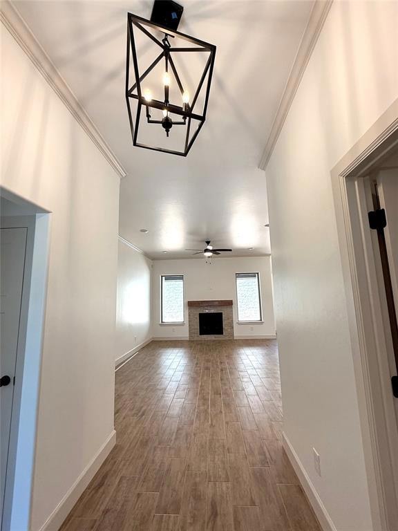 Unfurnished living room with baseboards, a ceiling fan, crown molding, wood finished floors, and a chandelier