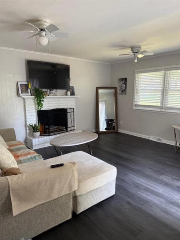 Living room featuring ceiling fan, crown molding, dark wood finished floors, and a brick fireplace