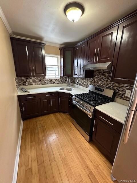 Kitchen featuring dark brown cabinetry, appliances with stainless steel finishes, ornamental molding, and tasteful backsplash