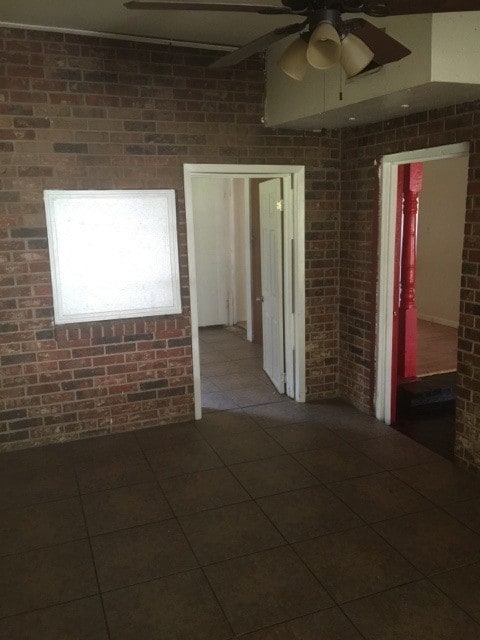 Spare room featuring brick wall, a ceiling fan, and dark tile patterned flooring