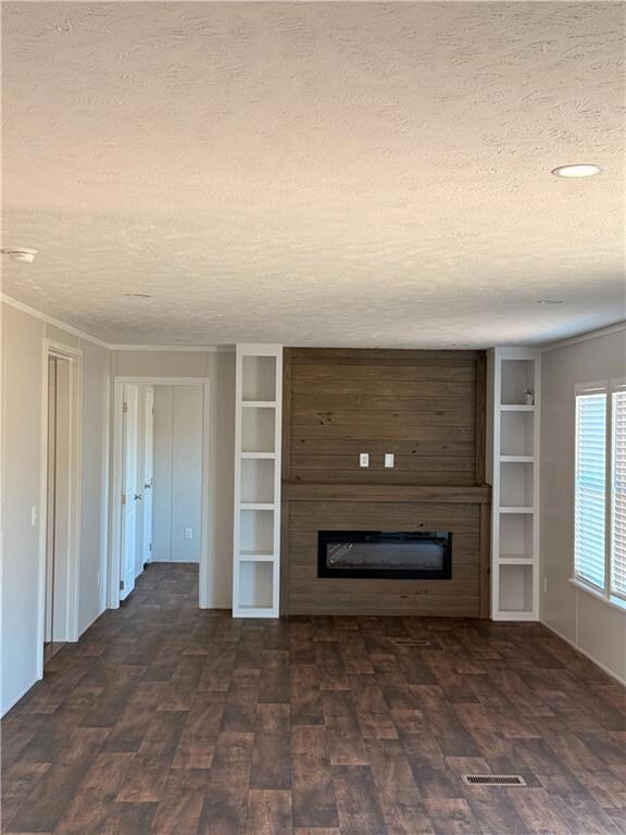Unfurnished living room with a glass covered fireplace, a textured ceiling, and built in shelves