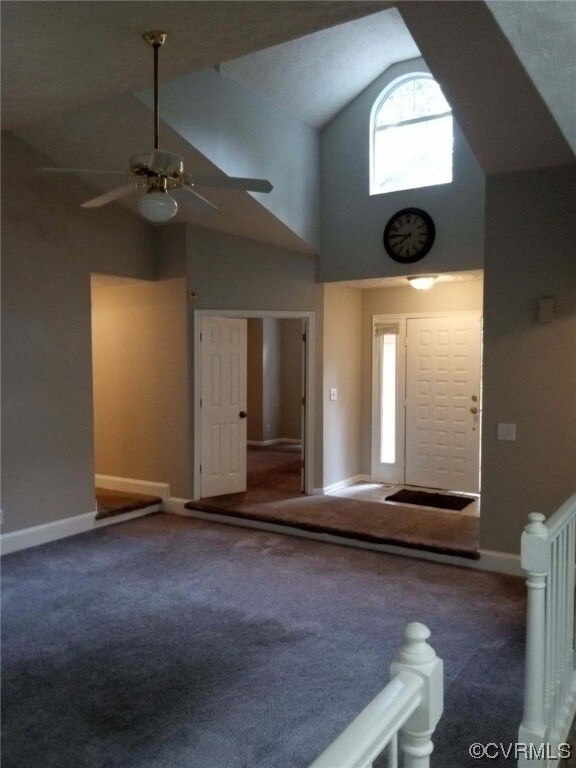 Interior space with vaulted ceiling high, dark colored carpet, and ceiling fan