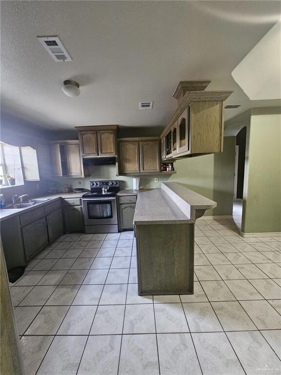 Kitchen with kitchen peninsula, exhaust hood, stainless steel electric stove, sink, and light tile floors