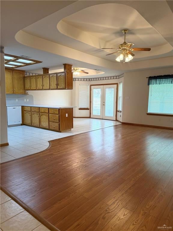 Unfurnished living room featuring a tray ceiling, light wood-type flooring, ceiling fan, and french doors