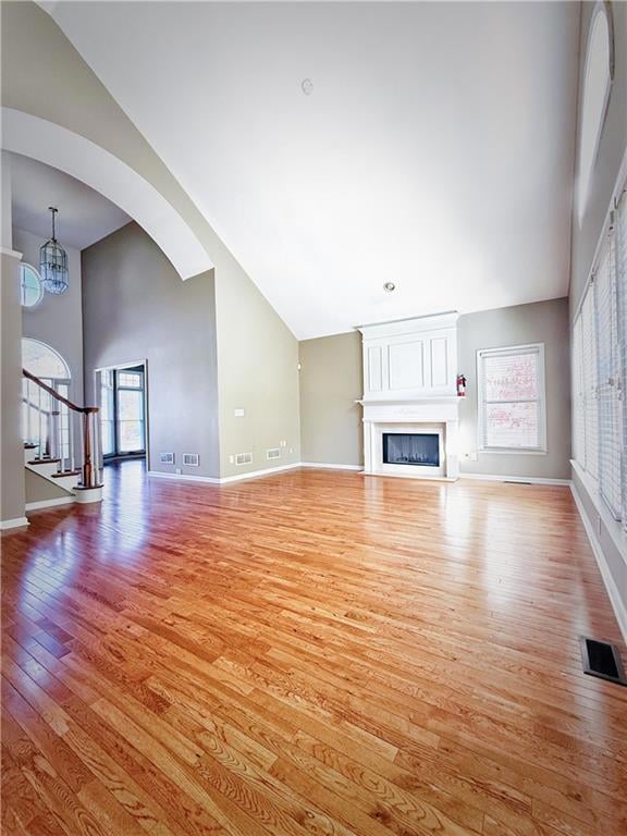 Unfurnished living room with light wood-style flooring, stairway, high vaulted ceiling, a fireplace, and arched walkways