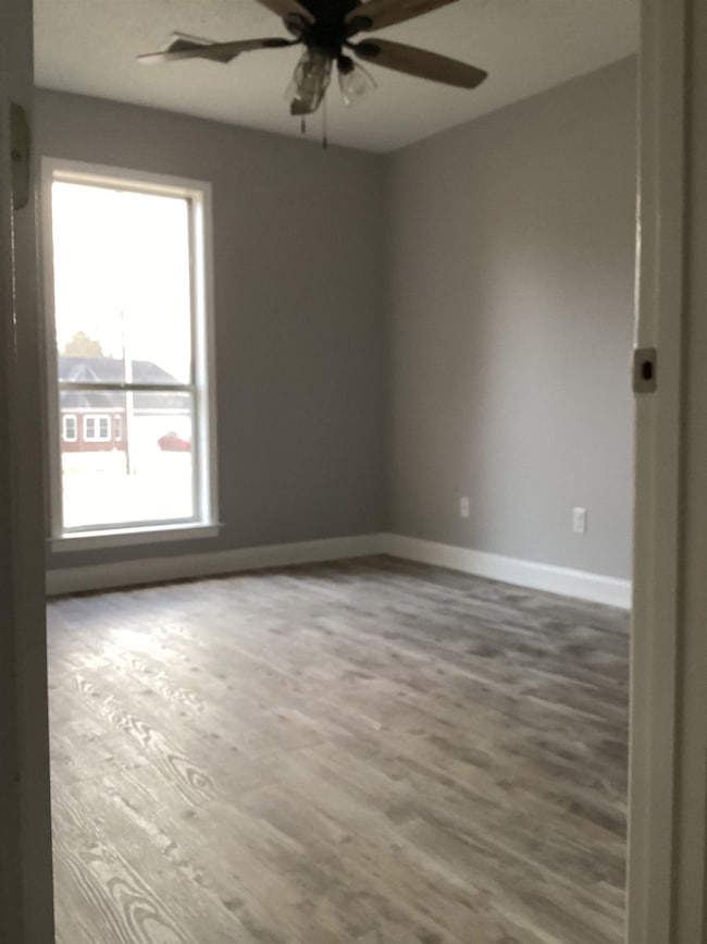Spare room featuring plenty of natural light, ceiling fan, wood finished floors, and baseboards