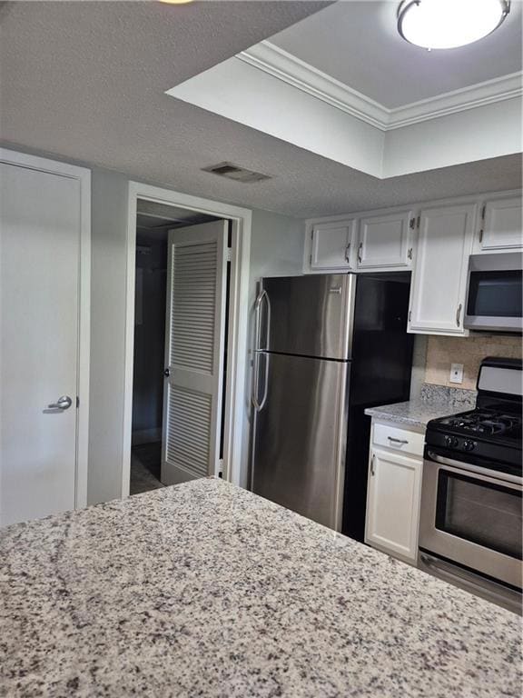 Kitchen with white cabinetry, stove, light stone counters, a textured ceiling, and fridge