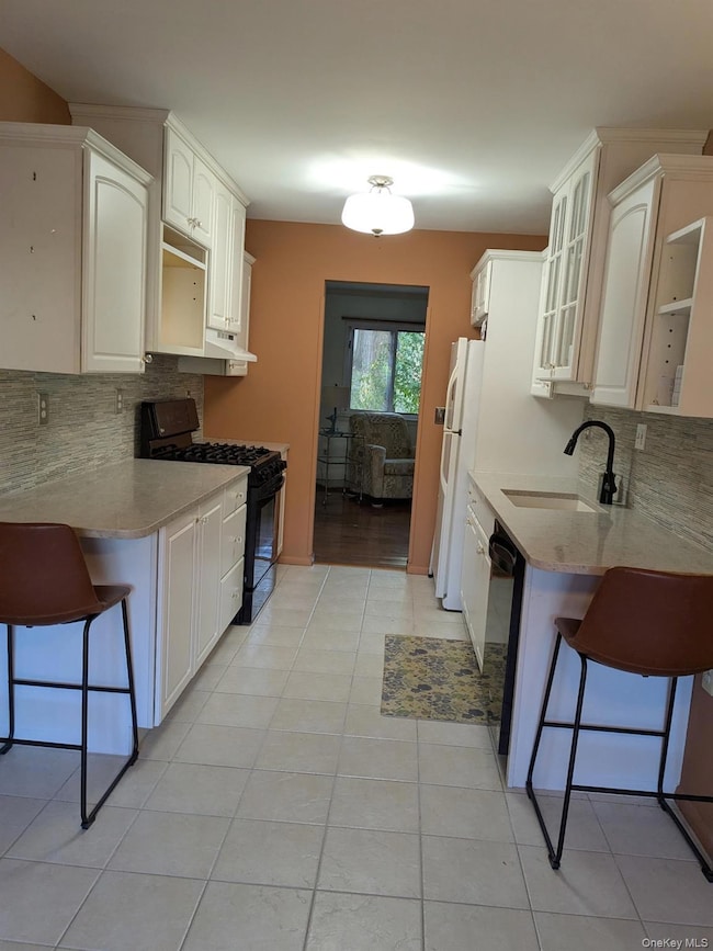 Kitchen with backsplash, a breakfast bar area, black appliances, and glass insert cabinets