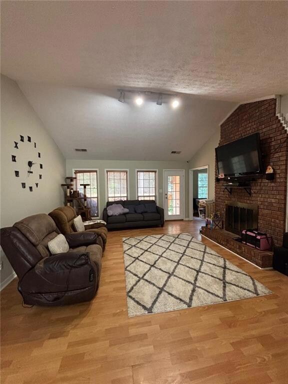 Living area featuring lofted ceiling, wood finished floors, a textured ceiling, and a fireplace