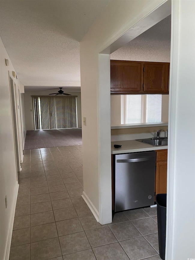 Kitchen featuring stainless steel dishwasher, dark tile patterned floors, light countertops, ceiling fan, and a textured ceiling
