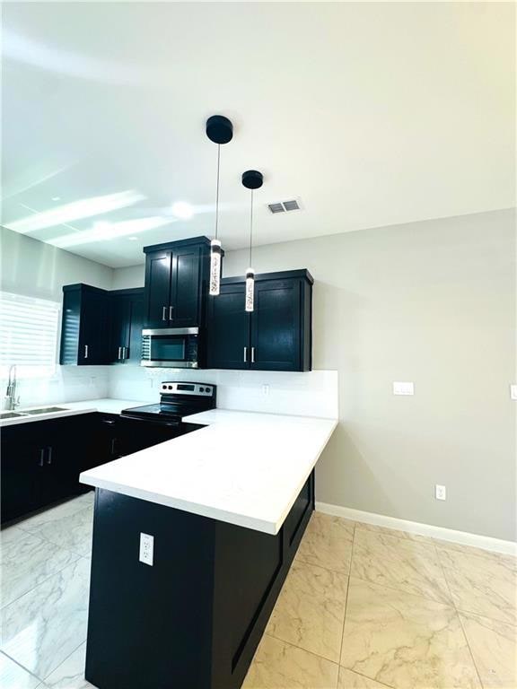 Kitchen with stainless steel appliances, light marble finish floors, a peninsula, dark cabinets, and light countertops