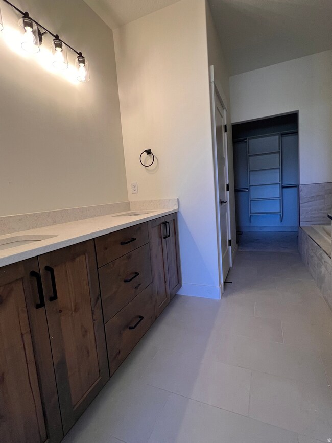 Bathroom with double vanity, tiled bath, and light tile patterned floors