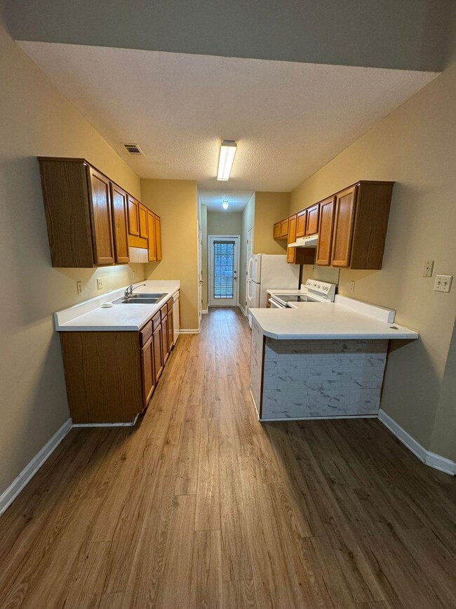 Kitchen with white appliances, a sink, baseboards, wood finished floors, and light countertops
