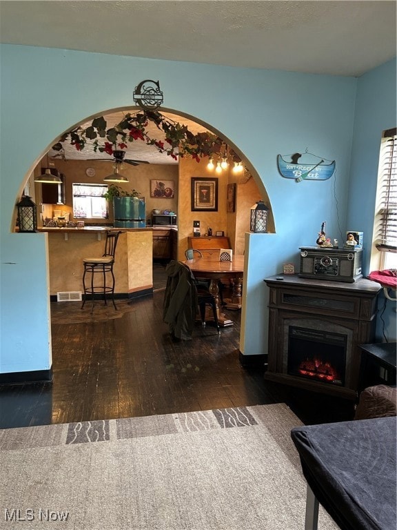 Living room featuring visible vents, arched walkways, a warm lit fireplace, and hardwood / wood-style flooring