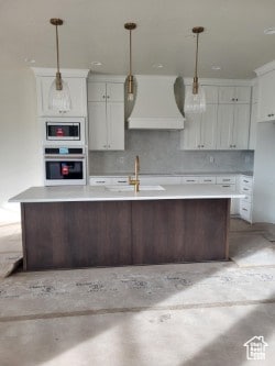 Kitchen with an island with sink, custom range hood, white cabinets, appliances with stainless steel finishes, and concrete flooring