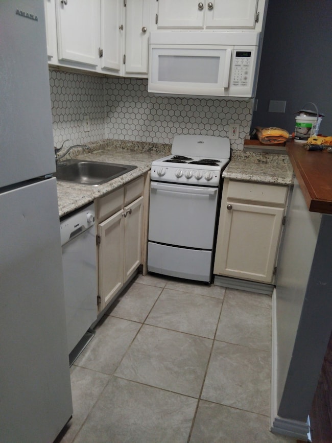 Kitchen featuring backsplash, white appliances, light tile patterned floors, and white cabinetry