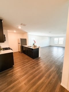 Kitchen featuring a peninsula, open floor plan, dark cabinetry, dark wood-type flooring, and light countertops