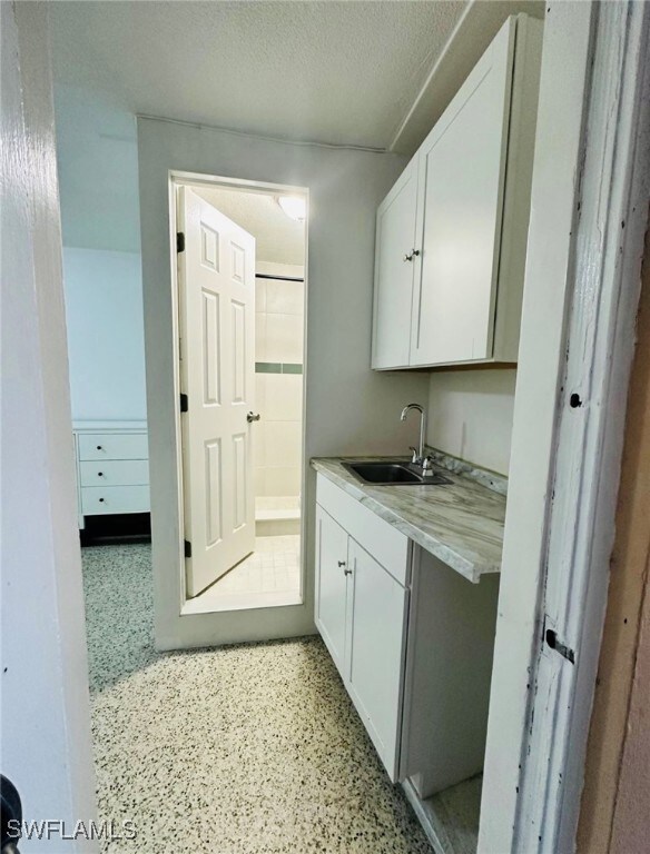 Kitchen with white cabinetry, sink, light stone co