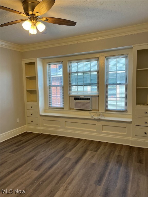 Empty room with ceiling fan, dark wood finished floors, ornamental molding, cooling unit, and a textured ceiling