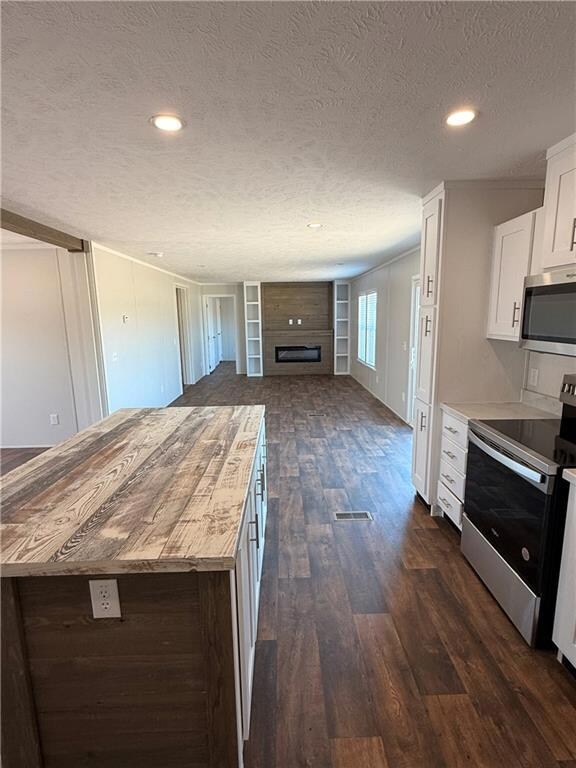 Kitchen featuring appliances with stainless steel finishes, a textured ceiling, open floor plan, white cabinets, and dark wood finished floors