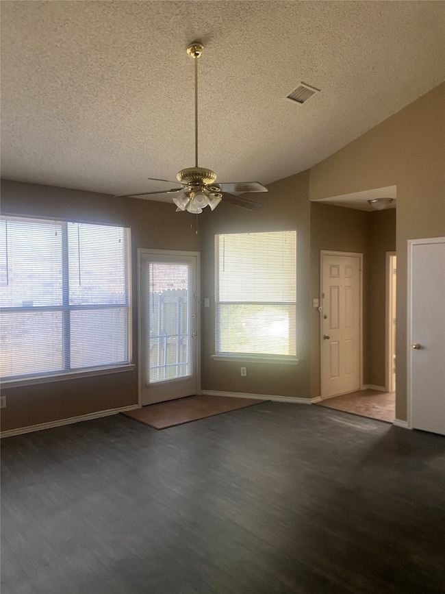 Unfurnished dining area with plenty of natural light, dark wood finished floors, a textured ceiling, vaulted ceiling, and ceiling fan