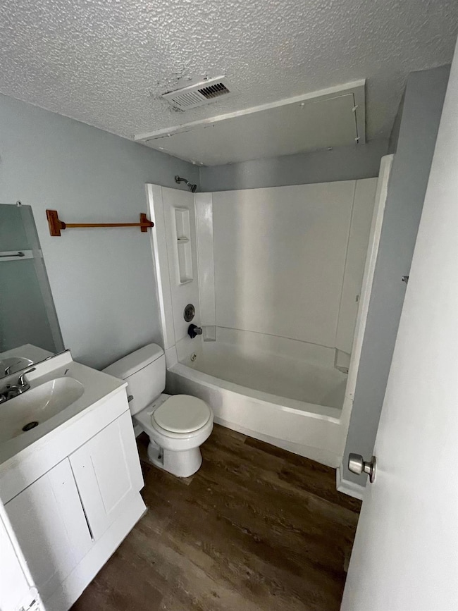 Full bath with wood finished floors, a textured c