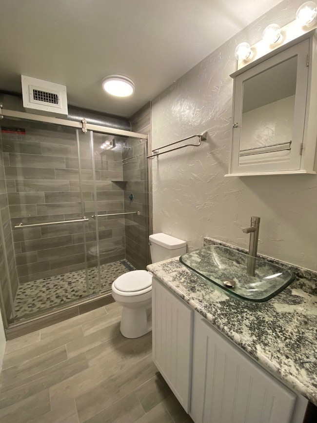 Full bath with a textured wall, vanity, a shower stall, and wood finish floors