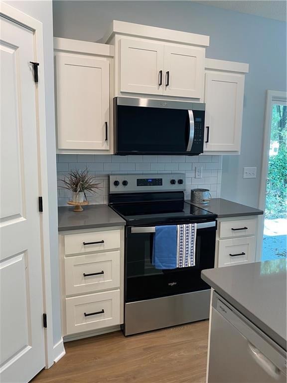 Kitchen featuring stainless steel appliances, white cabinets, decorative backsplash, and light wood-style floors