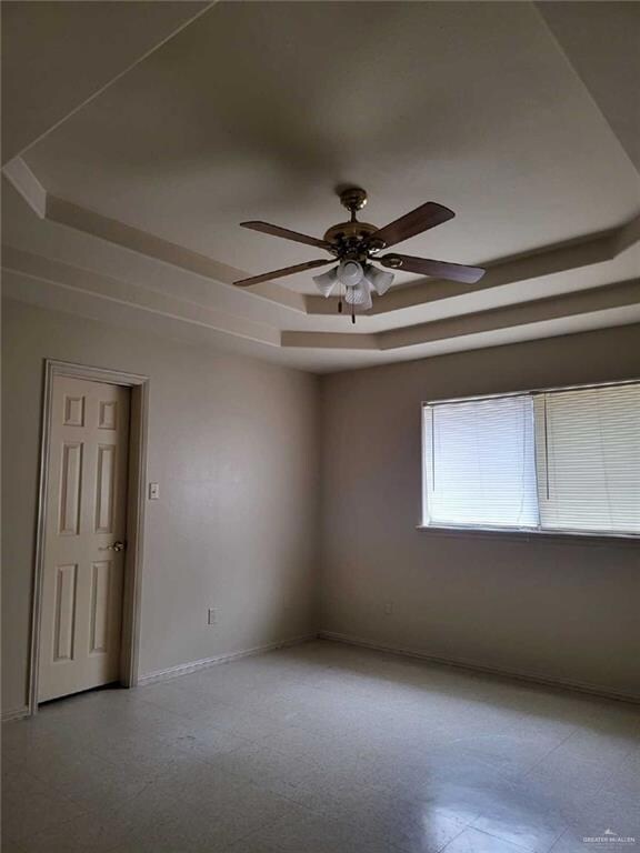 Empty room featuring baseboards, a tray ceiling, tile patterned floors, and ceiling fan