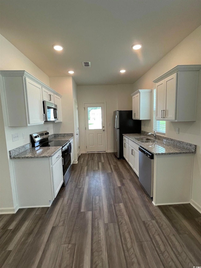 Kitchen featuring appliances with stainless steel finishes, dark wood-style flooring, recessed lighting, light stone countertops, and white cabinets