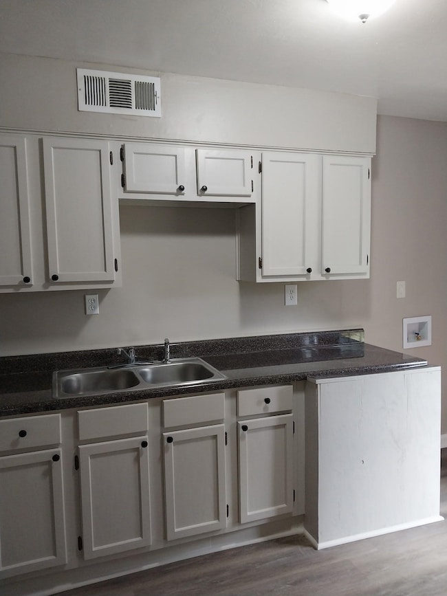 Kitchen with wood finished floors, dark countertops, and white cabinets