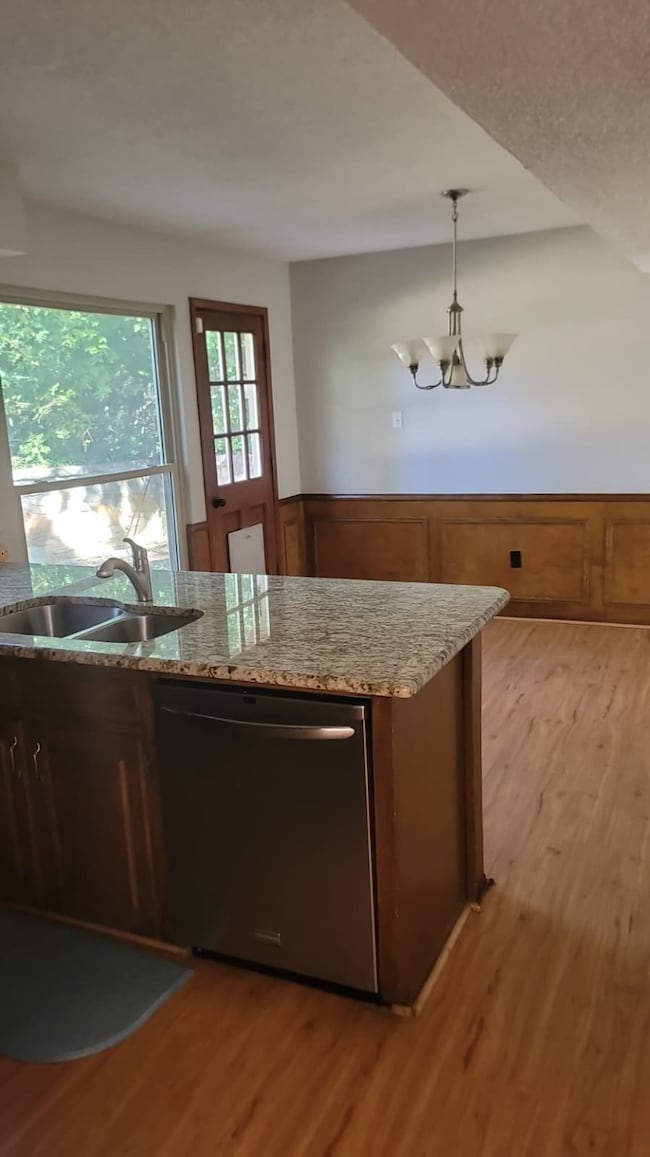 Kitchen featuring light wood-type flooring, stainless steel dishwasher, light stone counters, and a wainscoted wall