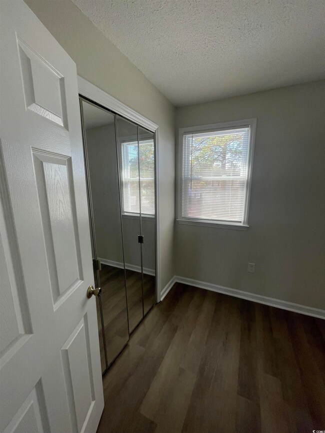 Unfurnished bedroom featuring a textured ceiling, dark wood-type flooring, and a closet