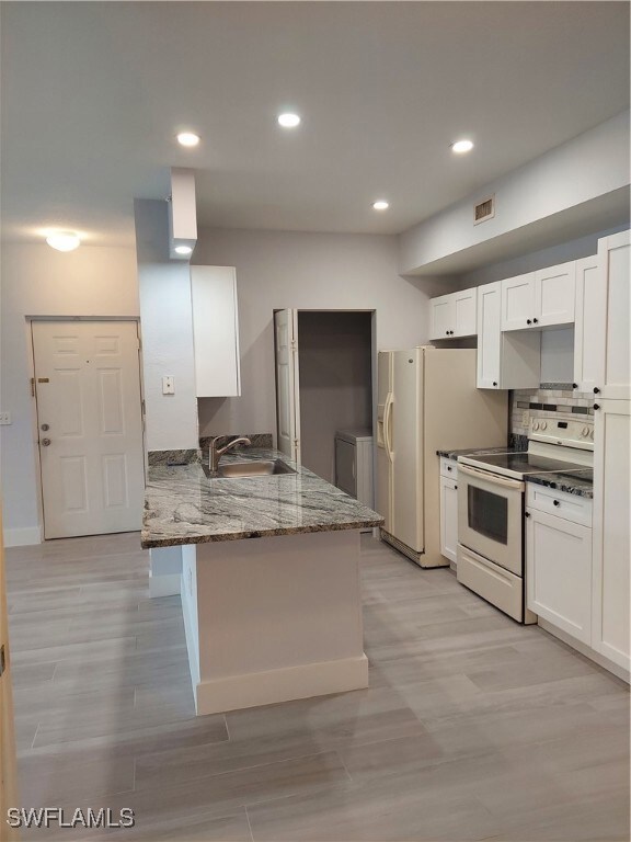 Kitchen featuring white range oven, dark stone countertops, white cabinets, a peninsula, and recessed lighting