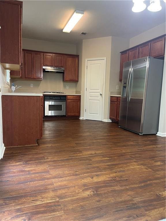Kitchen featuring appliances with stainless steel finishes, light countertops, dark wood-style floors, and under cabinet range hood