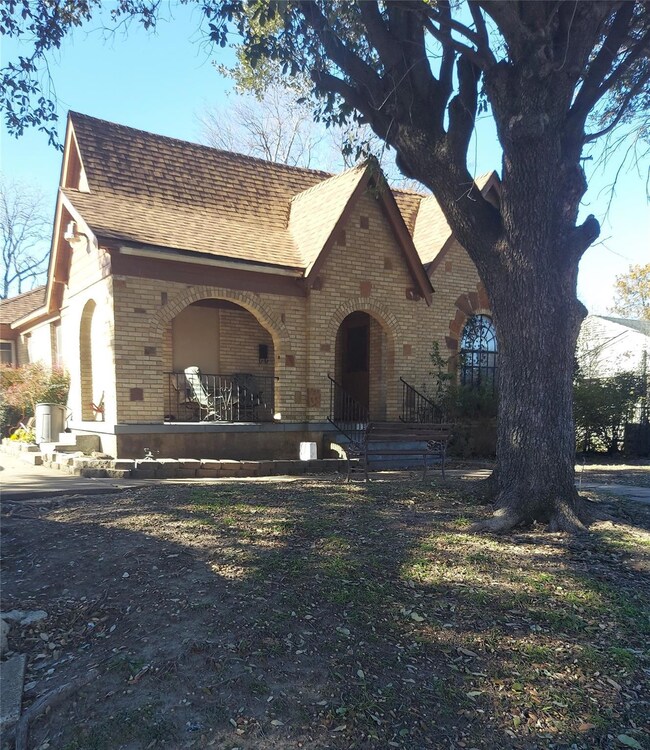 Tudor house featuring covered porch, roof with shingles, and brick siding