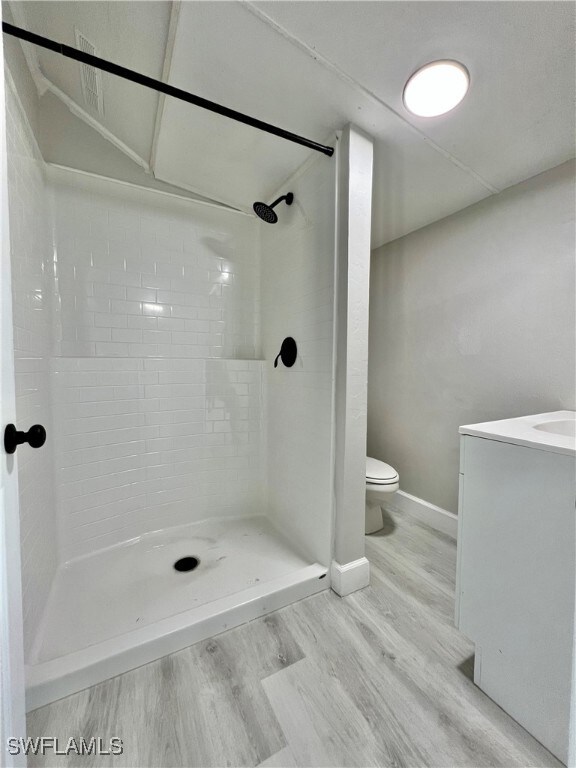 Bathroom featuring baseboards, toilet, a stall shower, wood finished floors, and vanity