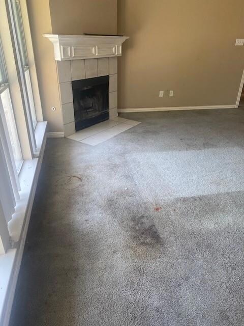 Unfurnished living room with a tiled fireplace and light colored carpet