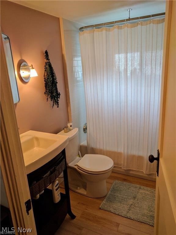 Full bathroom featuring toilet, hardwood / wood-style flooring, shower / tub combo with curtain, and vanity