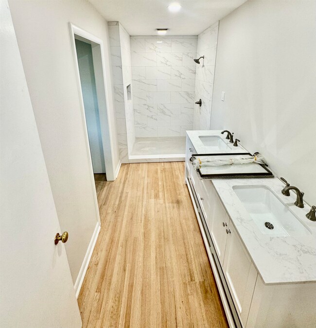 Full bathroom featuring a tile shower, double vanity, and wood finished floors