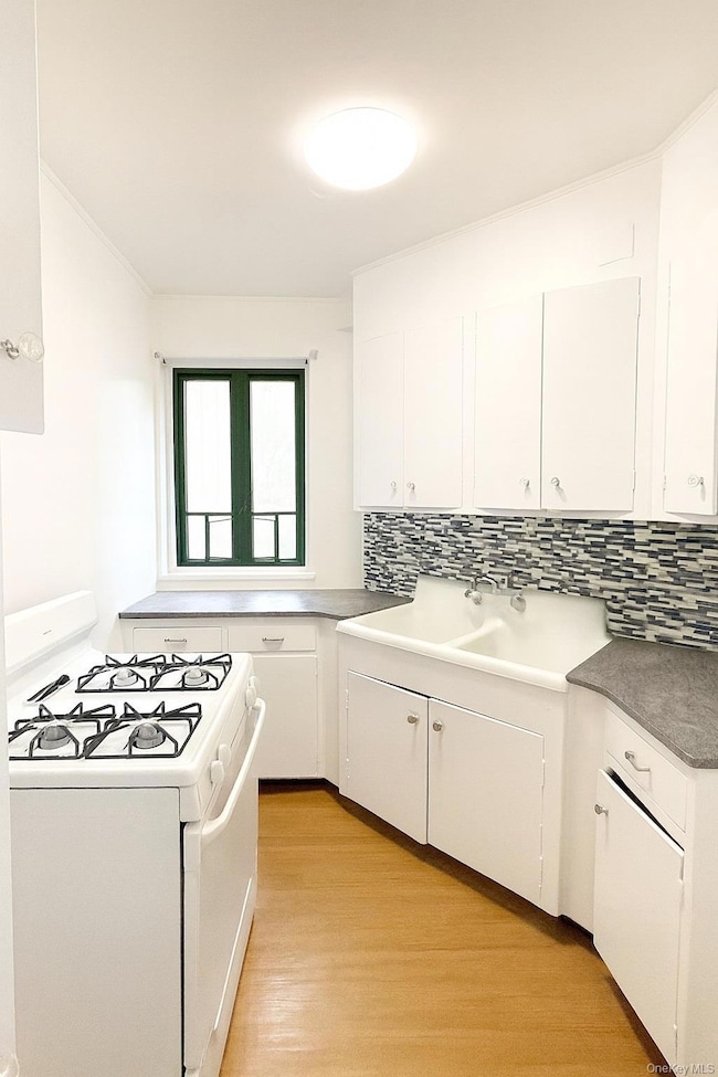 Kitchen with white range with gas stovetop, white cabinetry, light wood finished floors, tasteful backsplash, and dark countertops