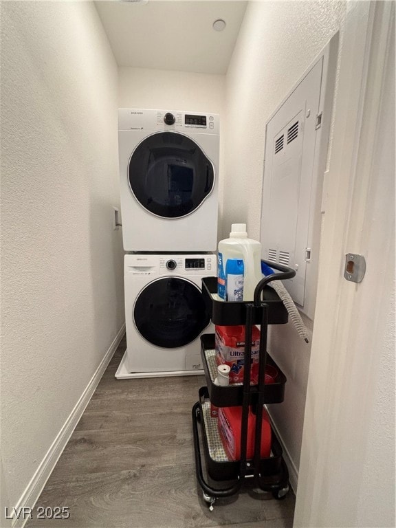 Laundry room with a textured wall, stacked washer / drying machine, and wood finished floors